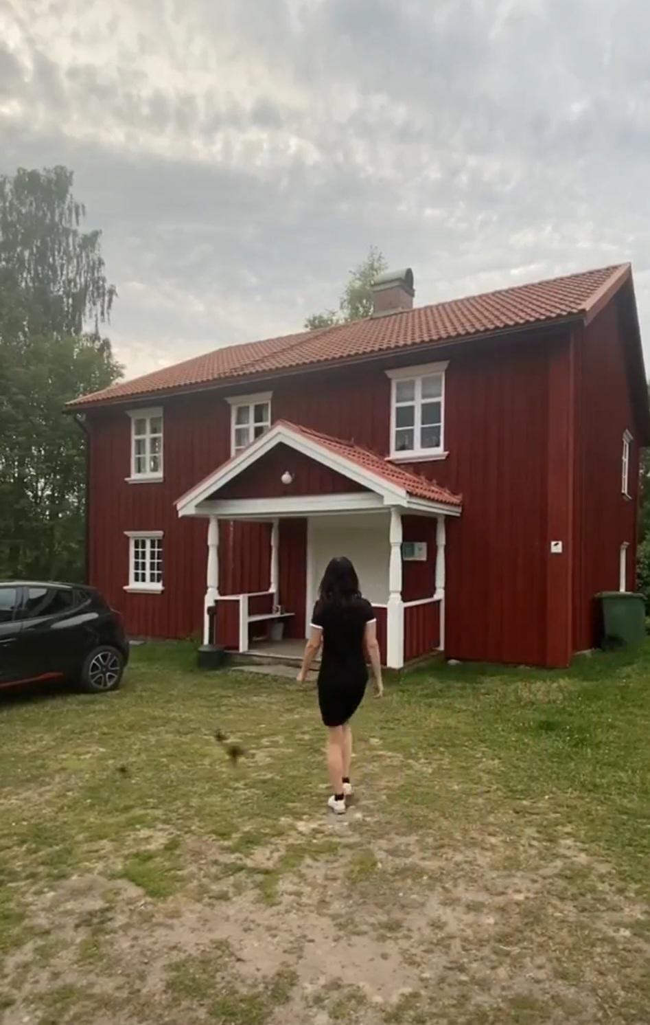 En person går över gräsmattan mot en röd tvåvåningsgård i skymningsljus