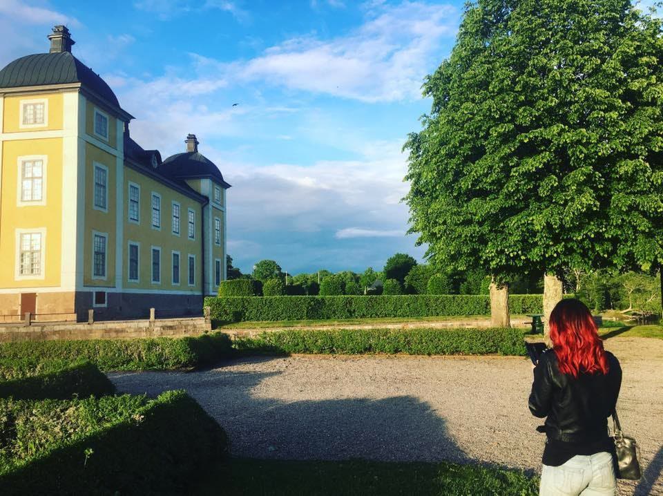 En person fotograferar ett gult slott i kvällssol från en grusplan kantad av häckar