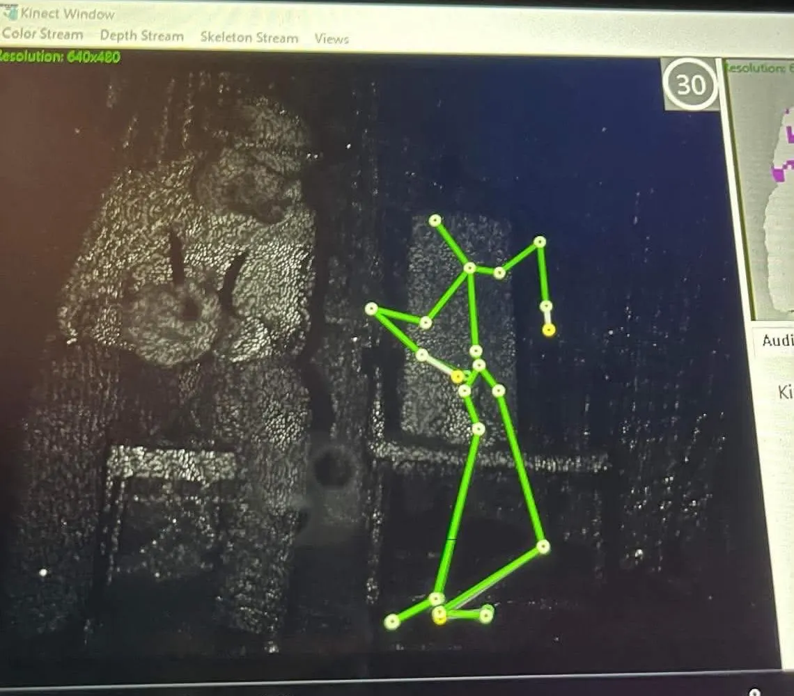 Skärmbild från en Kinect som ritar upp ett grönt skelett bredvid en stol i ett mörkt rum
