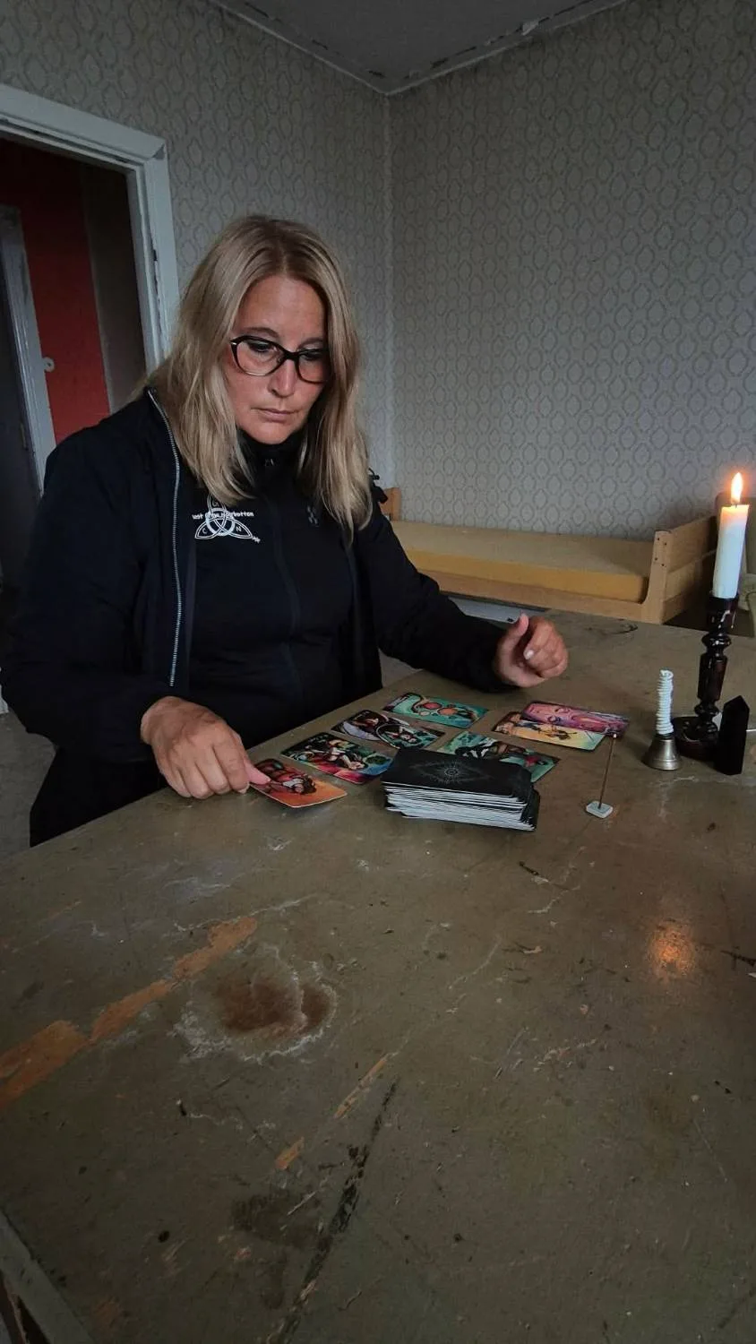 En kvinna lägger tarotkort på ett slitet bord i ett tomt rum, med ett tänt stearinljus bredvid