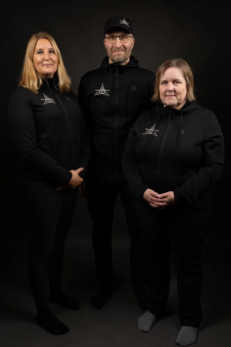 Tre personer i svarta tröjor med Ghost Crew Norrbottens logga, fotograferade mot svart bakgrund