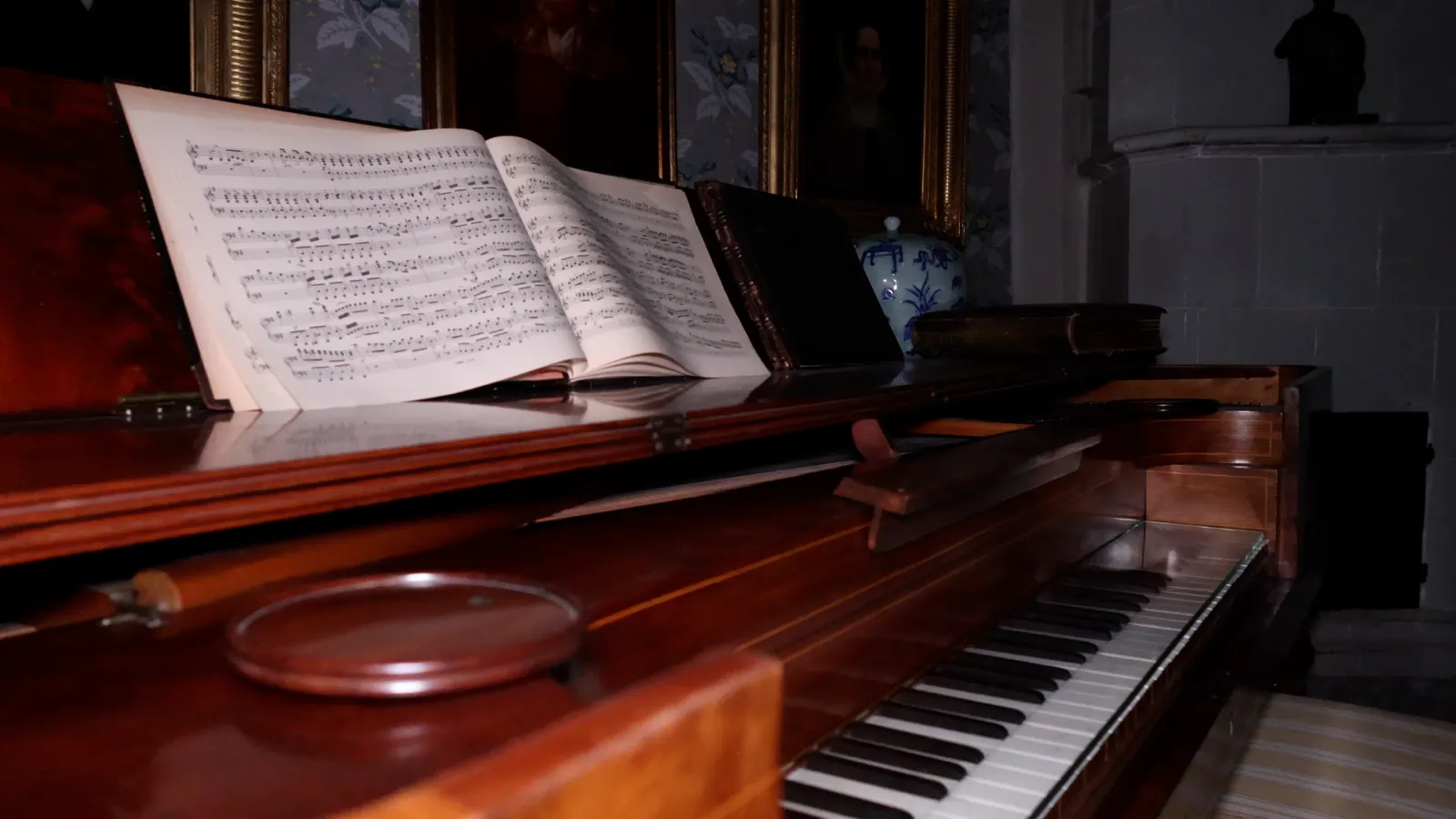Ett öppet piano med noter kvar på notstället i ett mörkt rum med gyllene tavelramar