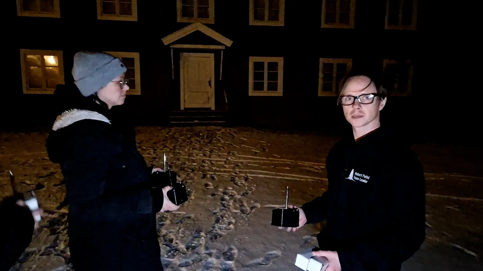 Ylva och Robert står utanför Gästgivars med varsin sensor i handen i nattmörkret