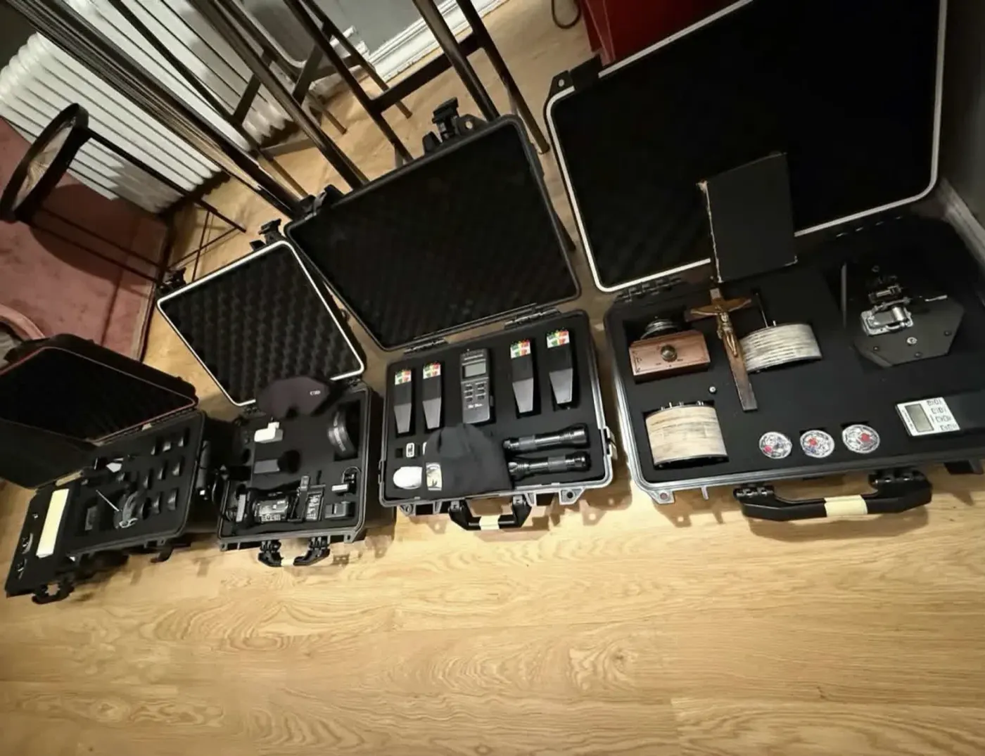 Fyra flightcase står uppslagna på golvet med mätare, ficklampor, ljudinspelare och ett kors.